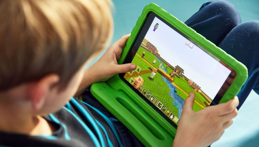 Criança focada e sorridente no joguinho. É possível aprender inglês com videogames no computador.