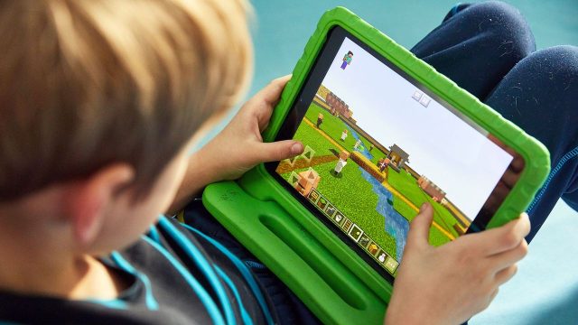 Criança focada e sorridente no joguinho. É possível aprender inglês com videogames no computador.